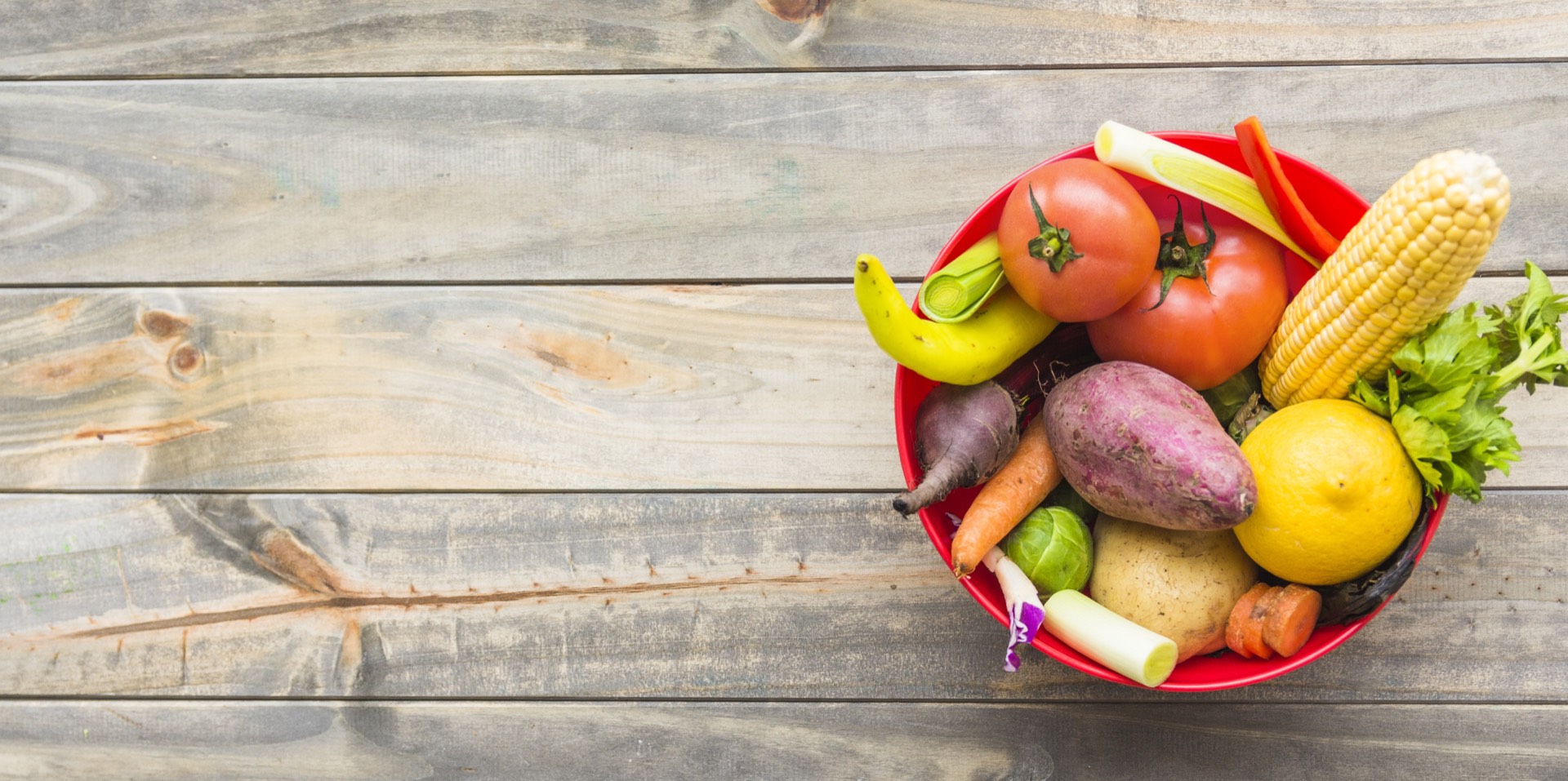 Bowl filled with fresh vegetables and fruit on a wooden table